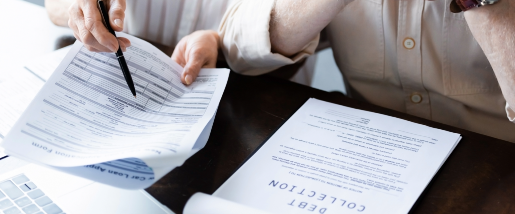 Hands holding a pen and reviewing debt collection paperwork.